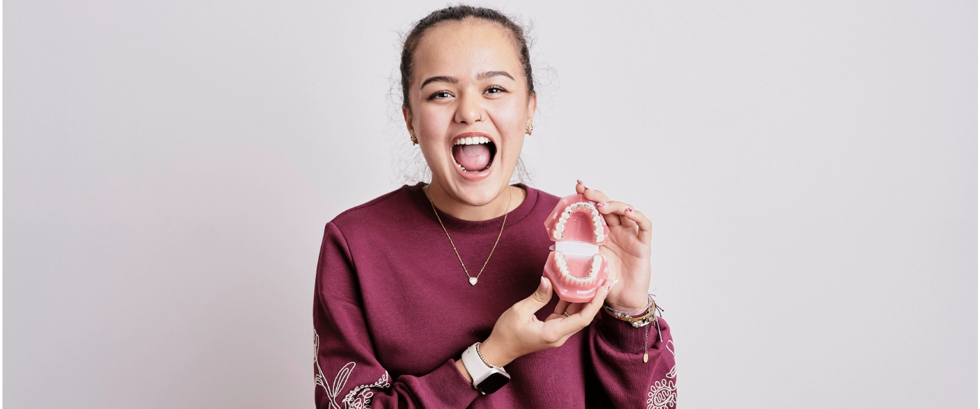 Teen is showhing her lingual braces and is happy.